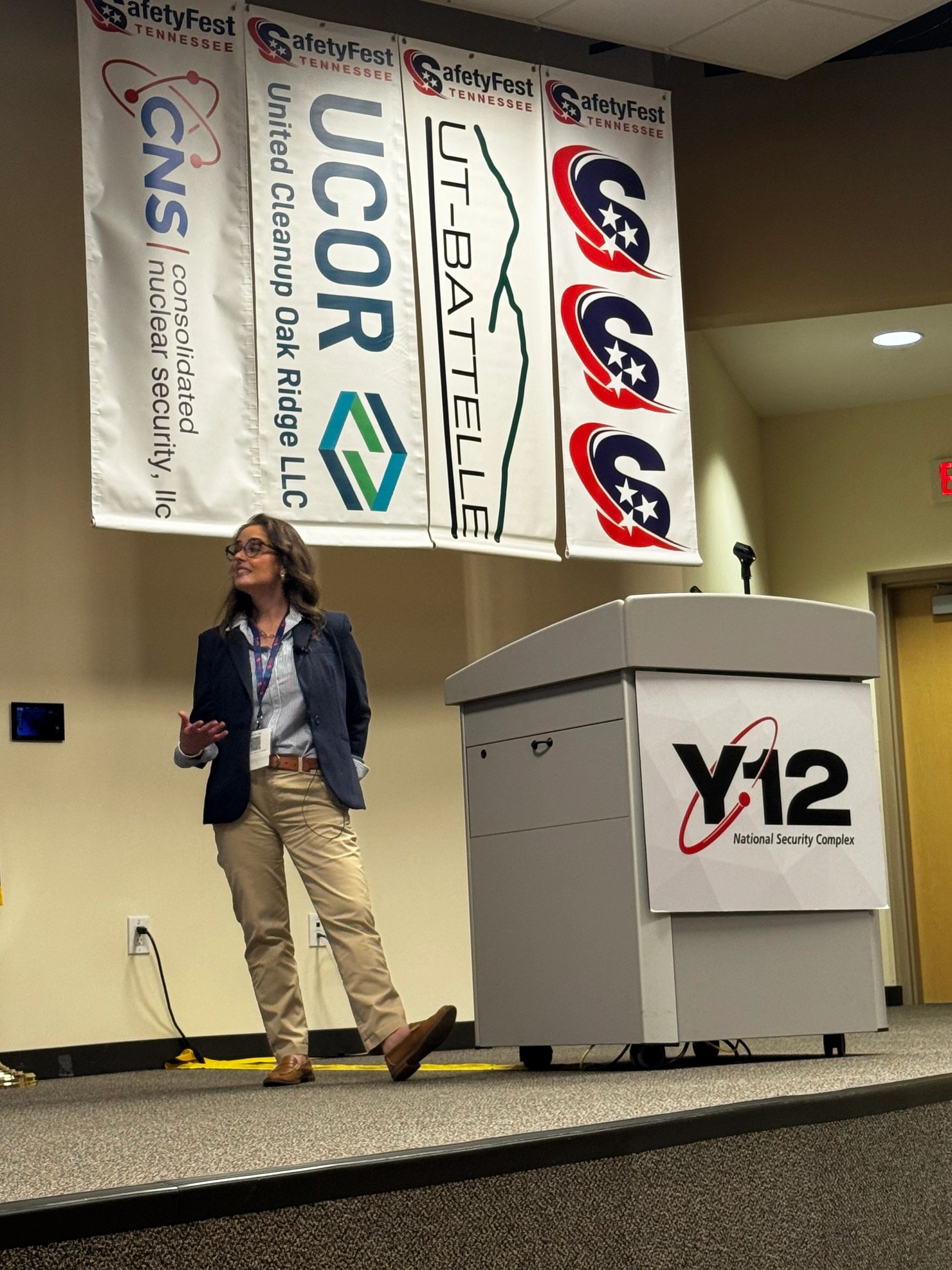 Aron Yellott speaking on stage at the y12 Nuclear facility in a navy blazer with khaki pants