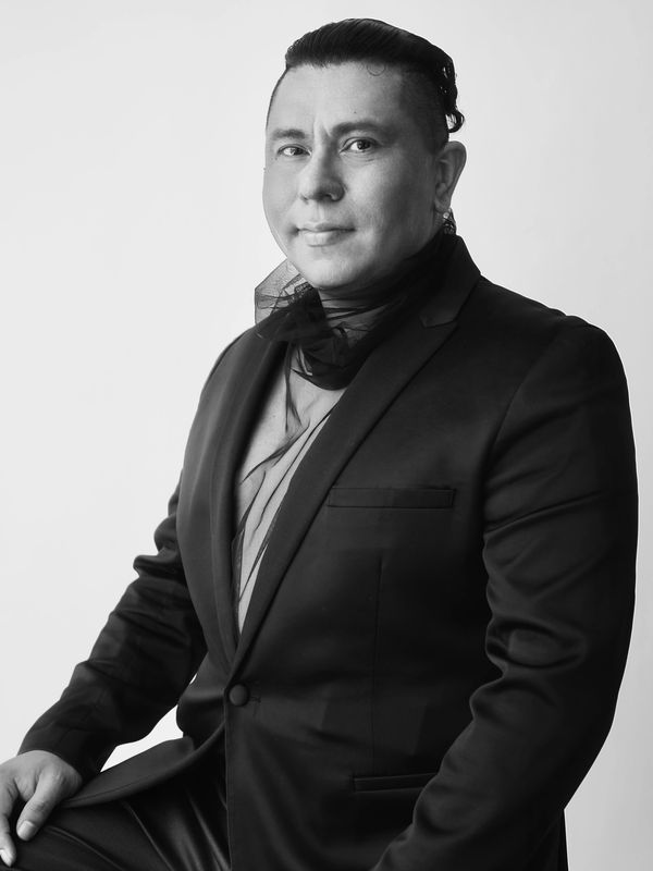 Monochrome portrait of a man in a suit with a sheer scarf, posing confidently.