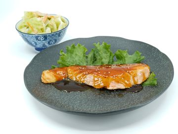 Glazed salmon fillet on lettuce with a side of salad in a blue bowl.