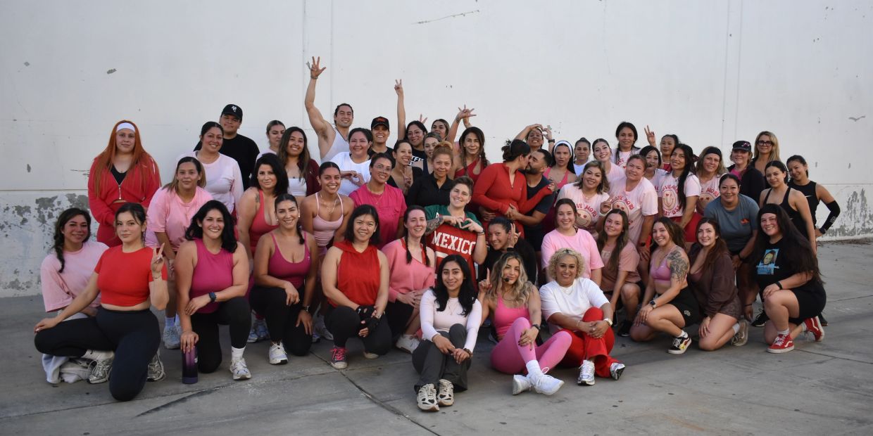 Large group of women posing outdoors against a white wall.