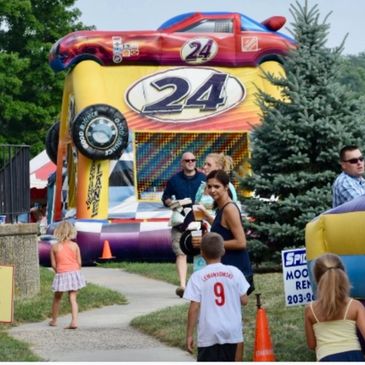 Children and adults enjoy a colorful carnival setting with a large inflatable race car attraction.