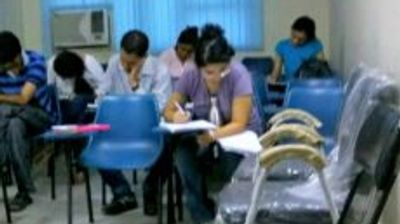 Students focused on writing in a classroom with blue chairs.
