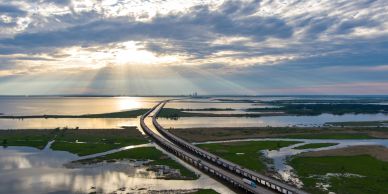 Train crossing over a water body under a cloudy sky.