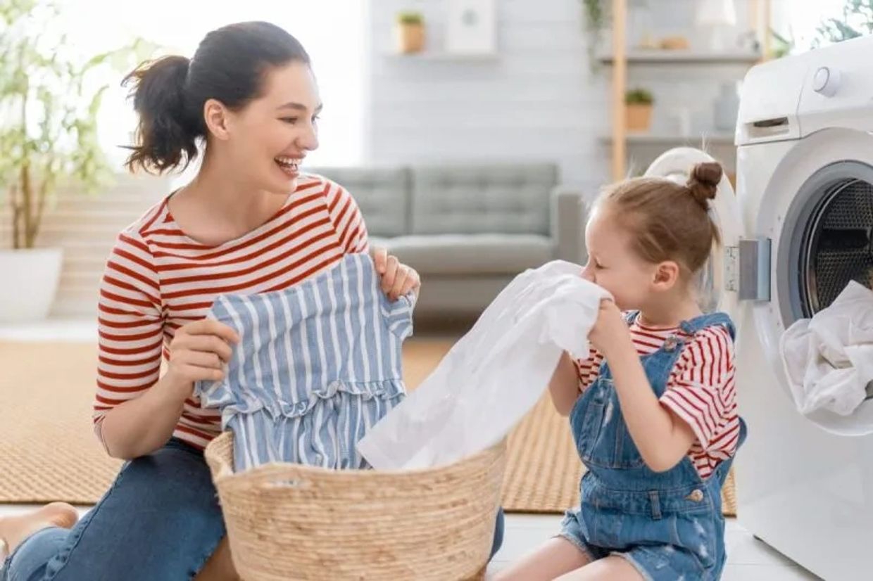Mother and daughter happily doing laundry together at home.