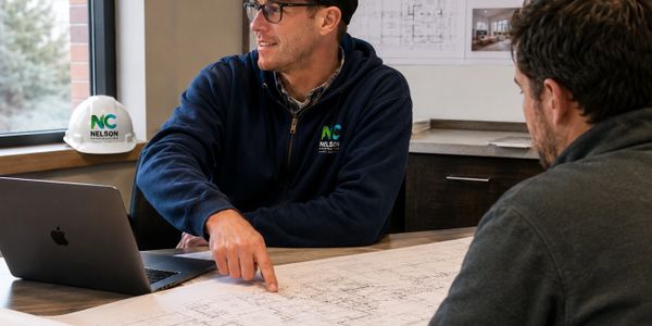 Two men discussing architectural plans at a table with a laptop and helmet.