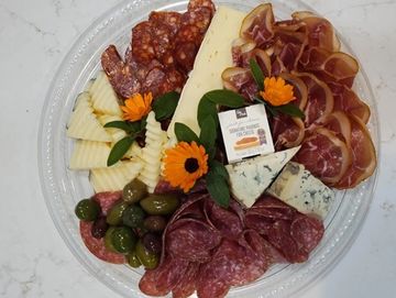 A charcuterie platter with assorted meats, cheeses, olives, and garnishes.