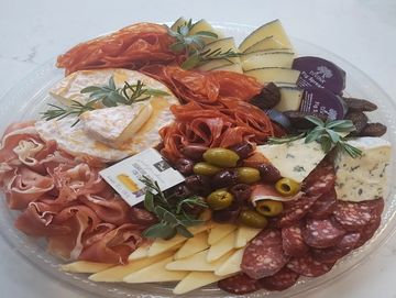 A platter with assorted cheeses, cured meats, olives, and herbs.