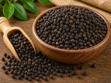 Black peppercorns in a wooden bowl and scoop on a rustic table.