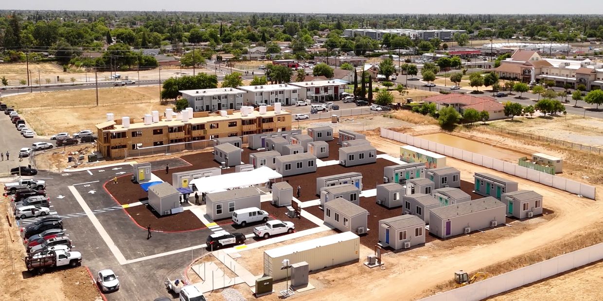 Aerial view of a temporary housing site with small modular units and a building under construction.