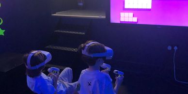 Two kids playing VR games with headsets and controllers in a dark room.