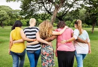 Five women standing arm-in-arm in a park, showing unity and friendship.