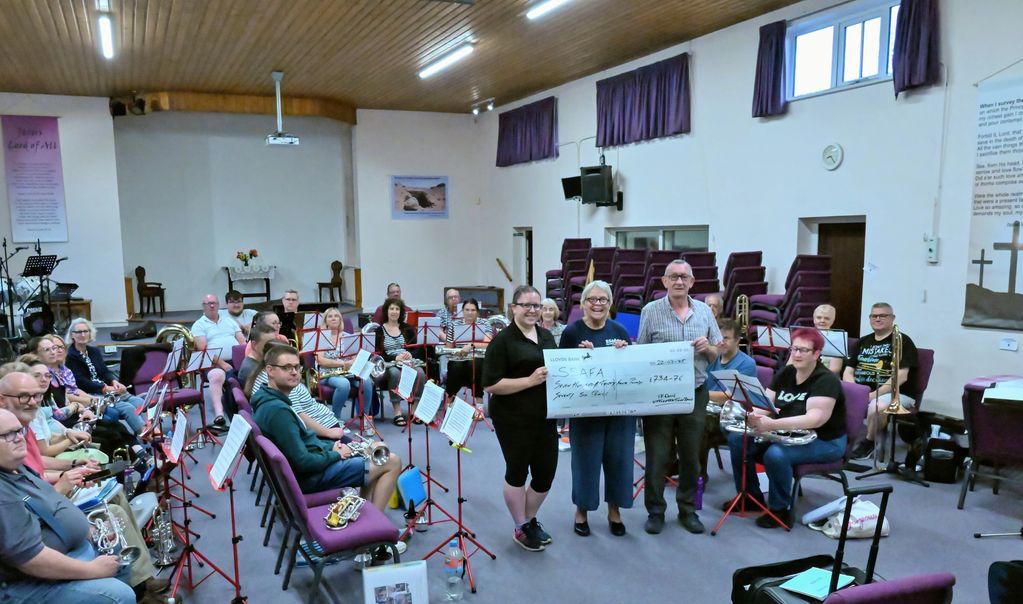 Group of musicians holding a large check in a rehearsal room.