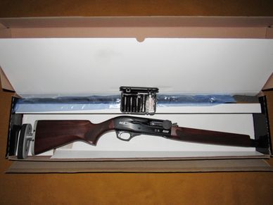 A shotgun with wooden stock in a box, accompanied by a cleaning kit.