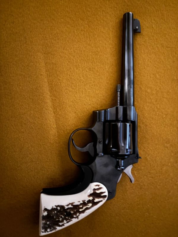 Black revolver with a white and brown textured handle on a mustard background.