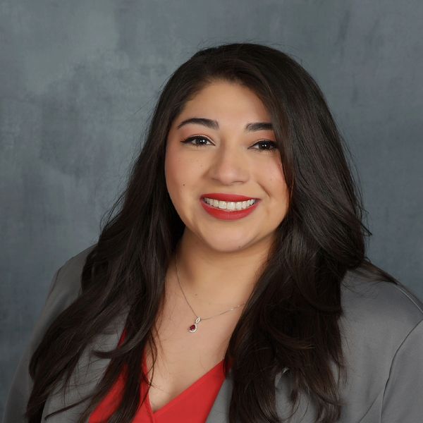 A woman with long dark hair smiling, wearing a gray blazer and red top.