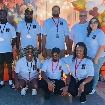 Group photo of eight people wearing matching light blue shirts at an outdoor event.