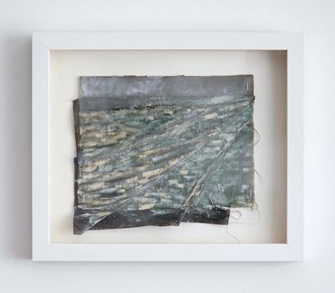 Framed abstract textile art with layered, weathered fabric in muted tones.