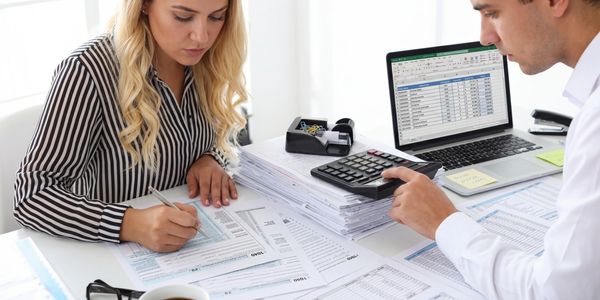 Two professionals reviewing financial documents and spreadsheets at a desk.