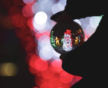 Christmas lights and a hand holding a glass sphere with a lit up snowman decoration in it.