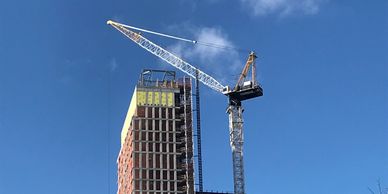 A tall construction crane working on a high-rise building under a clear blue sky.