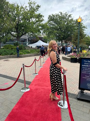 Woman poses on red carpet outdoors in polka dot dress.