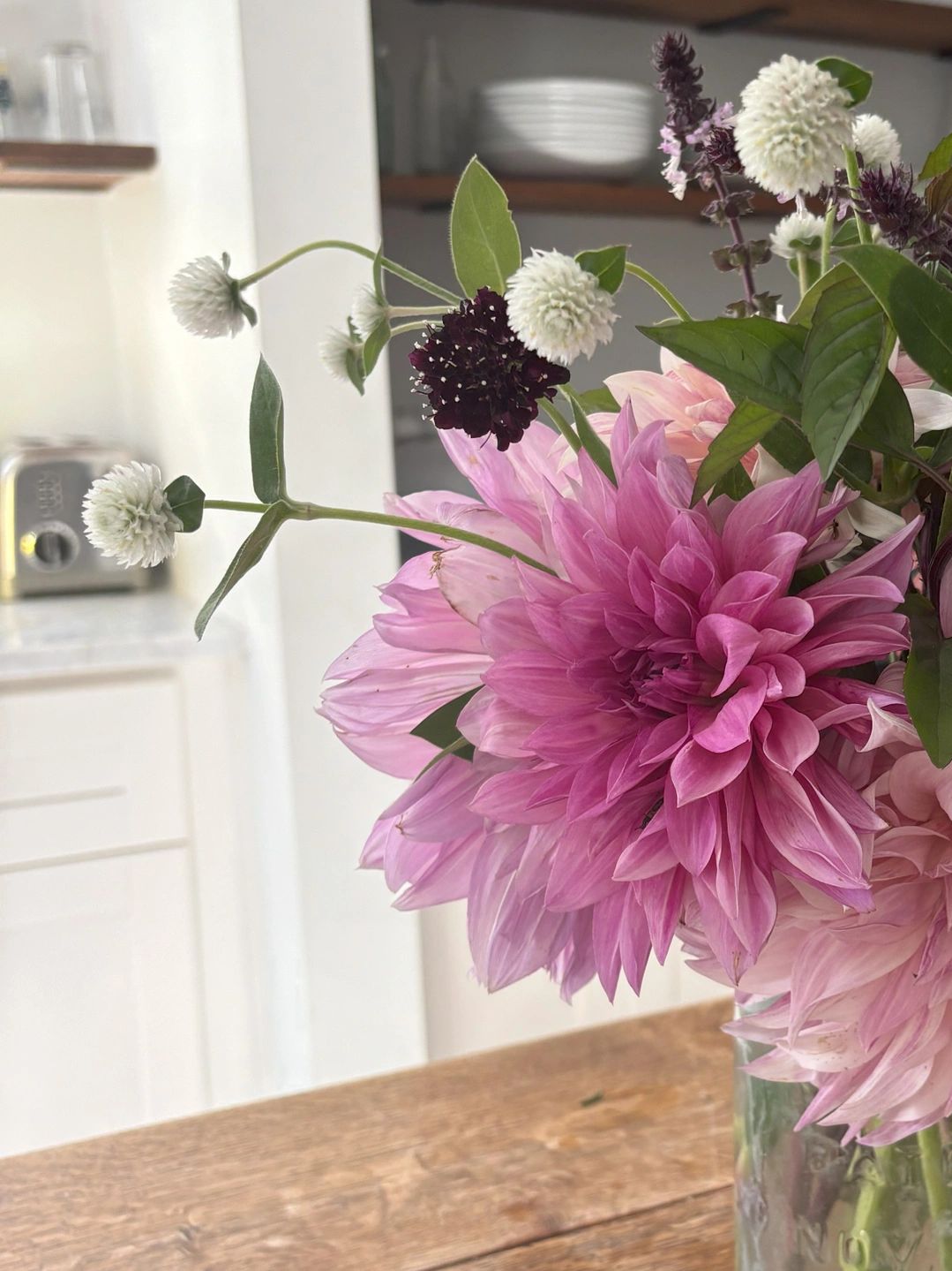 A bouquet of pink and white flowers in a glass jar on a wooden table.