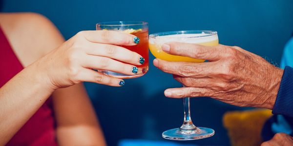 Two people clinking glasses with colorful cocktails in a celebratory toast.