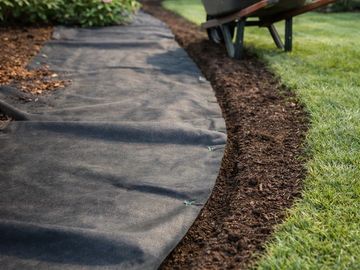 Garden path with landscape fabric being installed and a wheelbarrow of mulch.