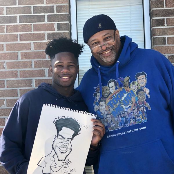 Two men smiling, one holding a caricature drawing of himself.