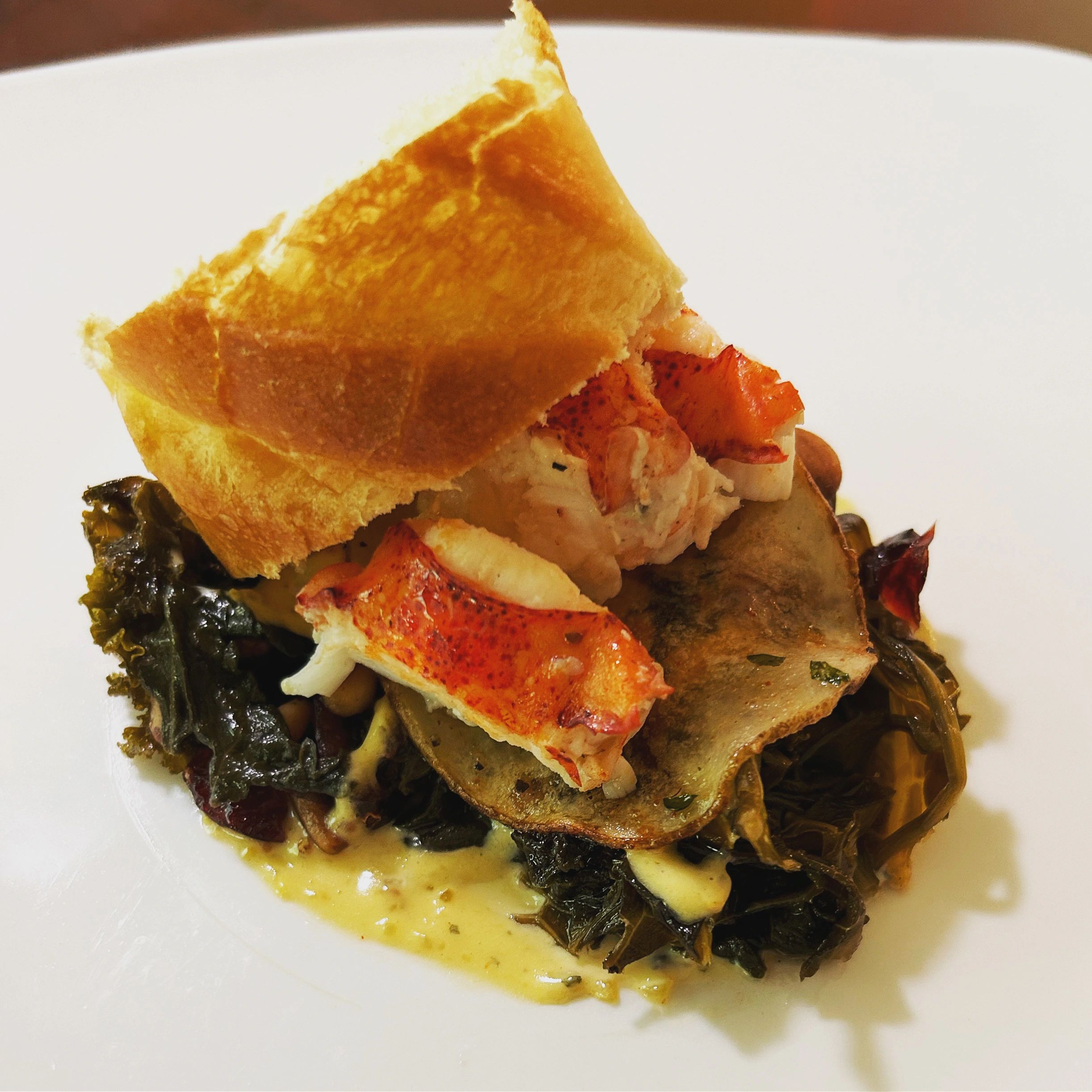 A deconstructed lobster roll with wilted kale and spinach on a pan seared potato and remoulade sauce