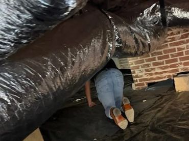 Person crawling through a narrow crawl space with brick walls and ducts.