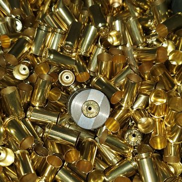 A large pile of shiny, brass bullet casings with one silver casing in the center.