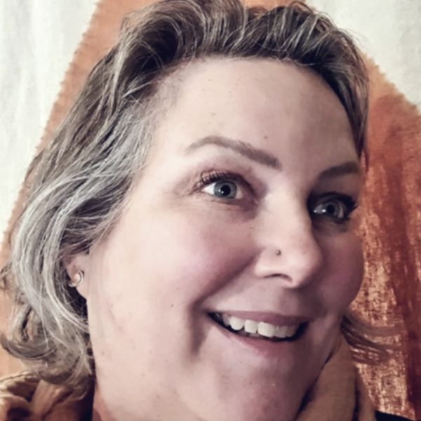 Close-up of a smiling woman with short hair and a nose piercing.