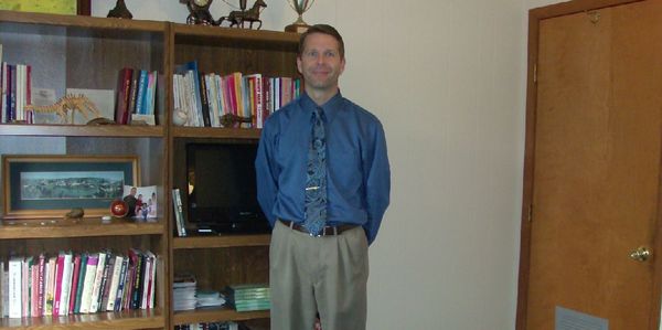 Man posing in a room with bookshelves and wooden doors.