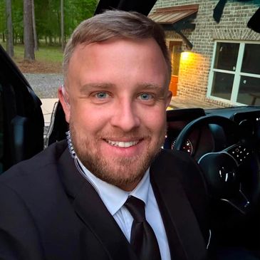 Smiling man in a suit sitting inside a car.
