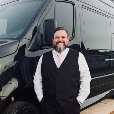 Smiling man in suit standing by a black van.