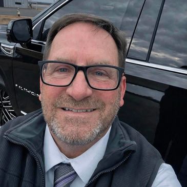 A man smiling in front of a black car.