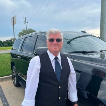Man in formal attire standing next to a black SUV.