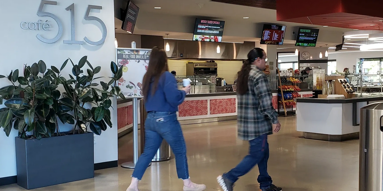 Two people walking into a corporate cafeteria.