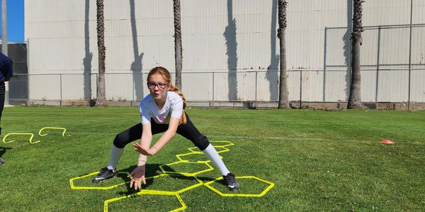 Young girl performing agility drills on a grass field with yellow hexagon markers.