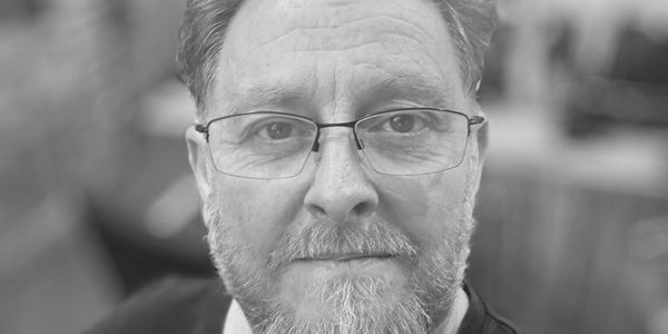 Middle-aged man with glasses and a reddish beard wearing a black shirt.