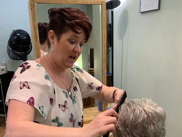 Hairdresser styling a client's short gray hair in a salon.