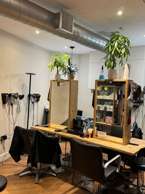 Modern hair salon with wooden stations, black chairs, and plants.