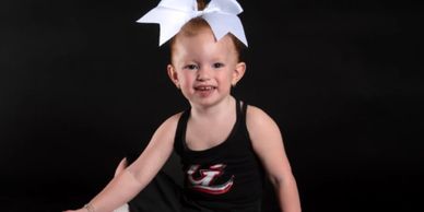 Smiling toddler with a white bow in her hair and a black outfit.