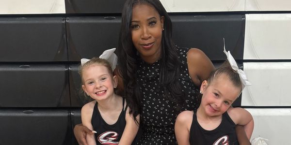 Woman posing with two young cheerleaders in black uniforms and white bows.