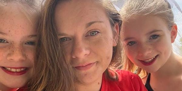A close-up selfie of a woman with two smiling young girls outdoors.