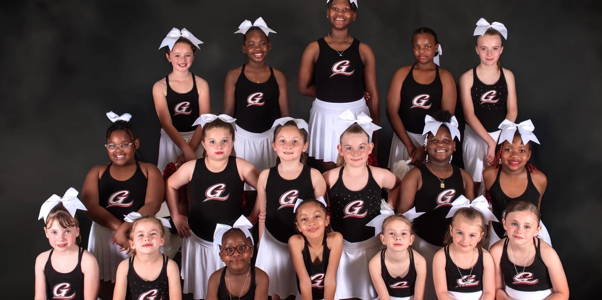 A group of young cheerleaders in black tops and white skirts posing.