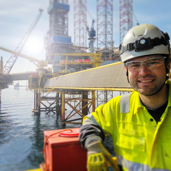 Smiling worker in safety gear at an offshore oil rig under sunny skies.