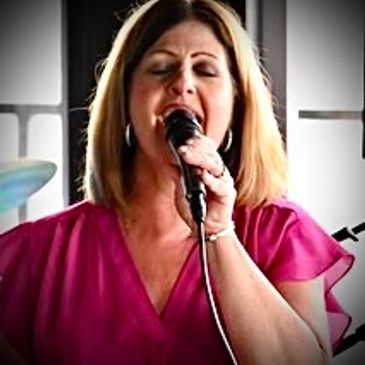 Woman passionately singing into a microphone indoors.