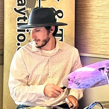 Man in a hat playing drums indoors.